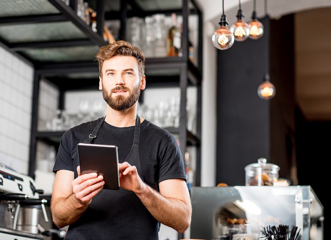 Business Insurance - Man Wearing a Black Shirt and Apron Using a Tablet to Check Inventory at a Bar