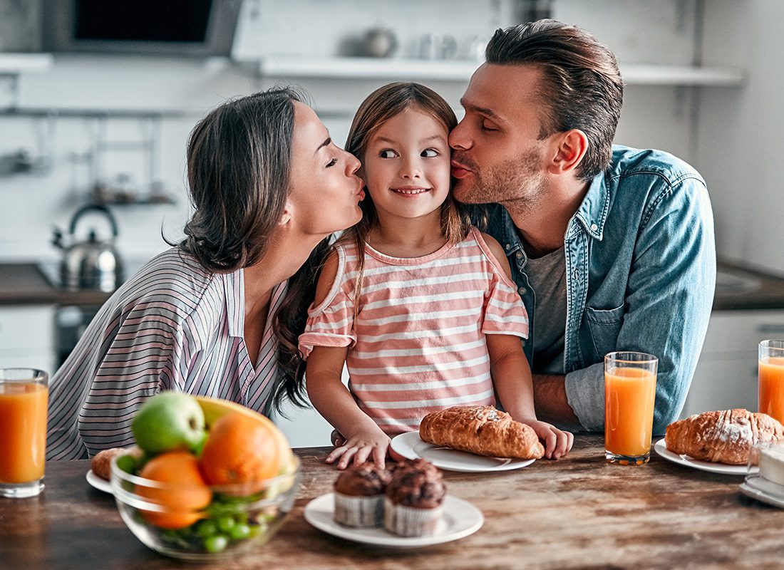 Personal Insurance - Mother and Father Kiss Their Daughter on Both Cheeks in the Kitchen During Breakfast