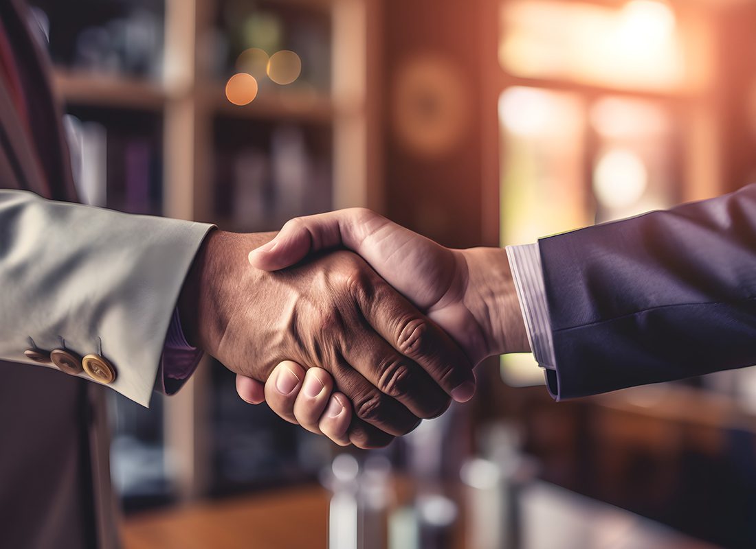 Our Business Partners - Close Up of Two Professionals Shaking Hands in an Office with Warm Light Coming in Through the Window